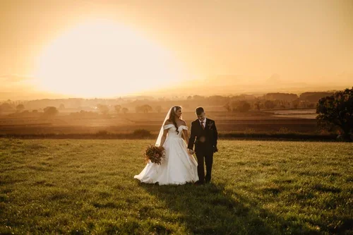 The newlyweds walking through a field in golden evening light.