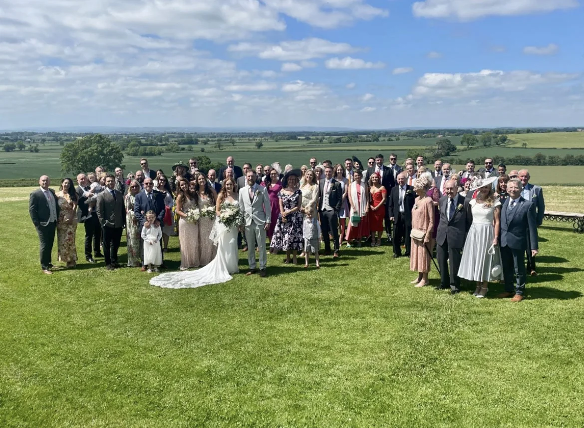 Wedding guests gathered with the couple for a group photograph on the lawn.