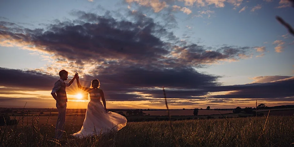 The newlyweds holding hands in silhouette against a dramatic sunset.