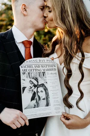 The newlyweds kissing while holding a personalised wedding newspaper.