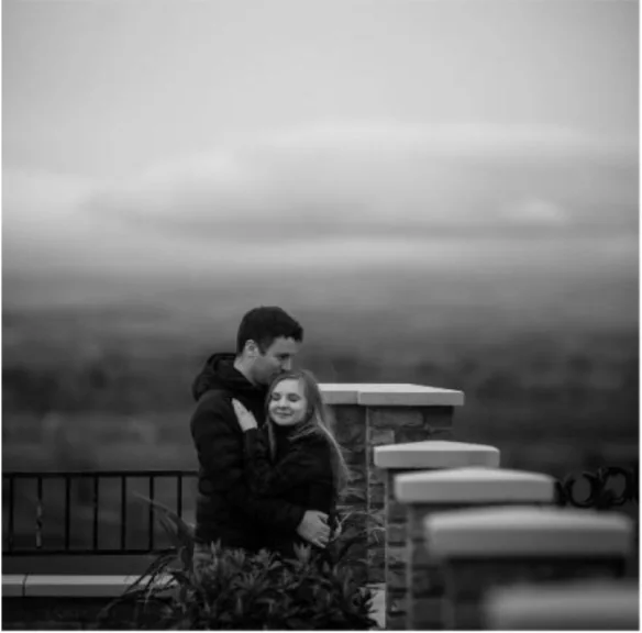A black-and-white portrait of a couple beside a stone wall overlooking the countryside.