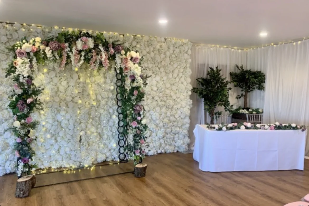 A floral ceremony backdrop, flower-covered arch and white-clothed signing table.