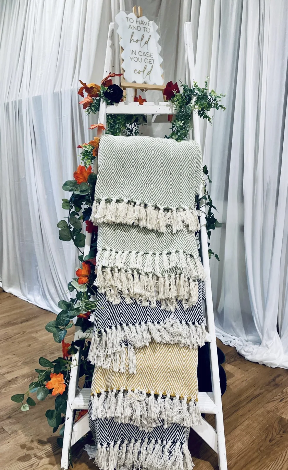 Folded blankets displayed on a ladder for wedding guests.