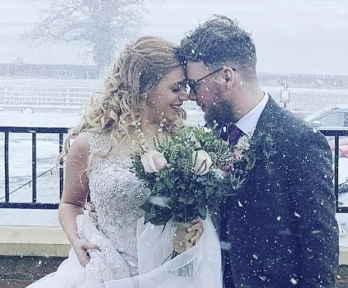 The newlyweds smiling together outdoors in falling snow.