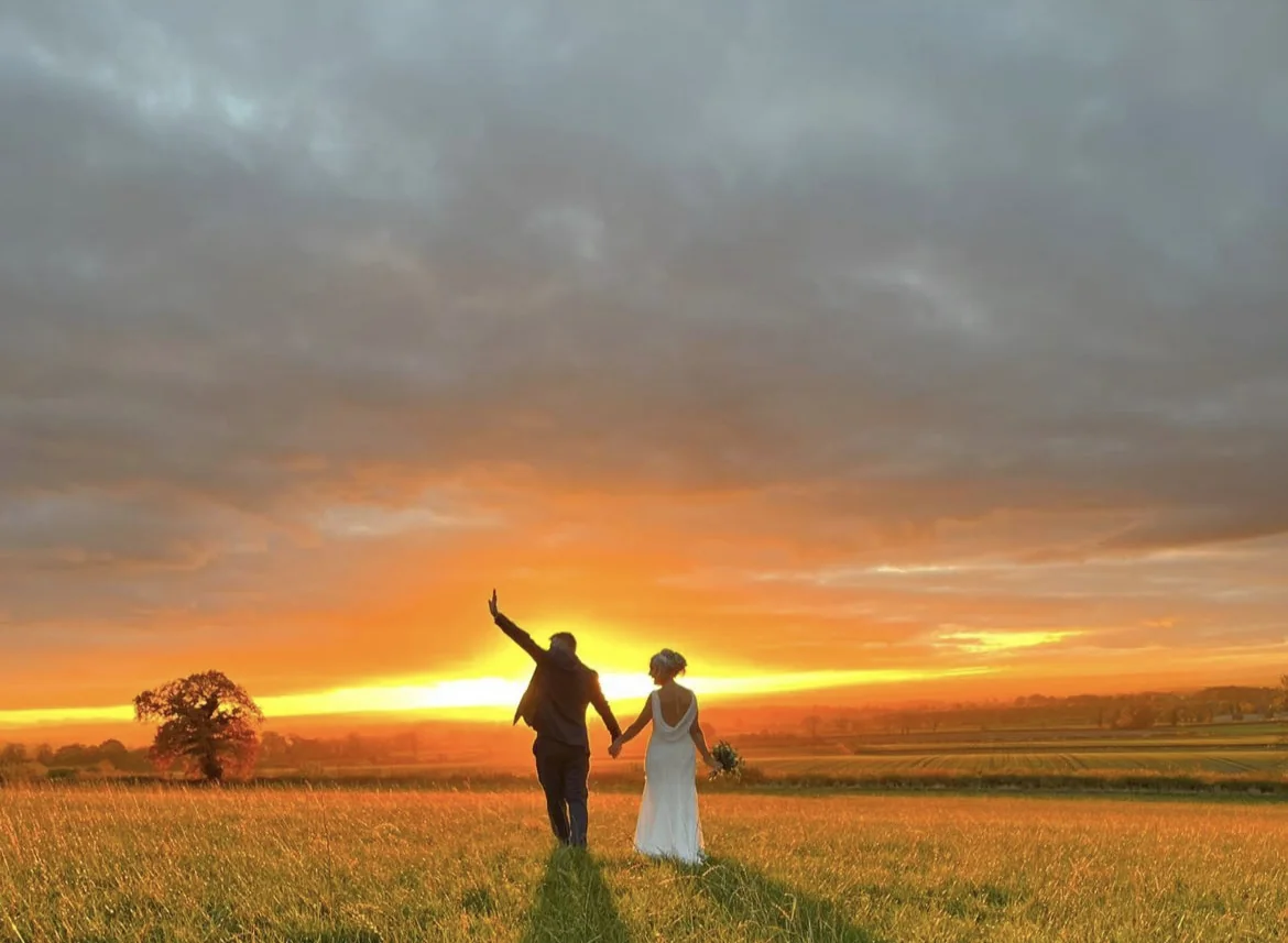 The couple celebrating in a field against a vivid orange sunset.