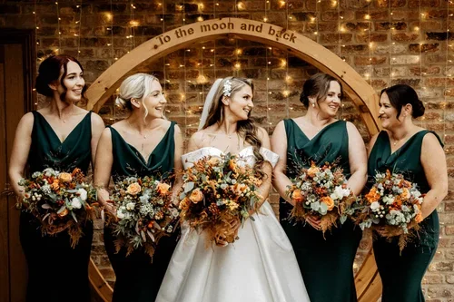 The bride and bridesmaids in green dresses holding autumn-coloured bouquets.