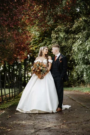 The newlyweds standing together on a tree-lined path.