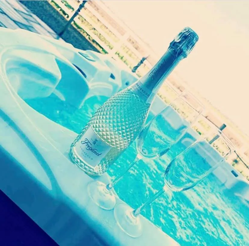 A bottle of sparkling wine and glasses beside a pool.