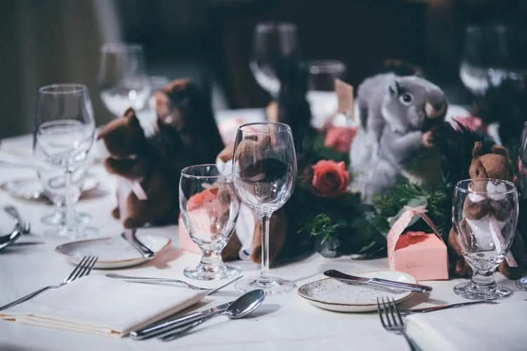 Wedding table settings with glasses, red flowers and small animal figures.