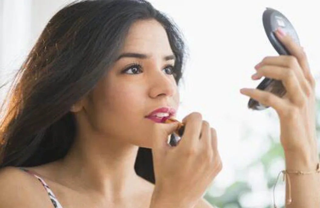 Applying lipstick while looking into a compact mirror.