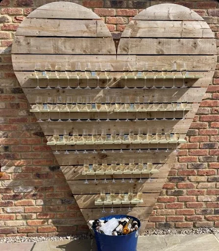 A large heart-shaped wooden display filled with small glasses against a brick wall.