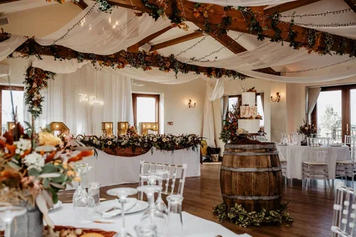 Wedding reception tables beneath white draping and autumn foliage, with a cake on a barrel.