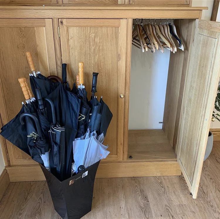 Umbrellas stored beside a wooden wardrobe for guests to use.