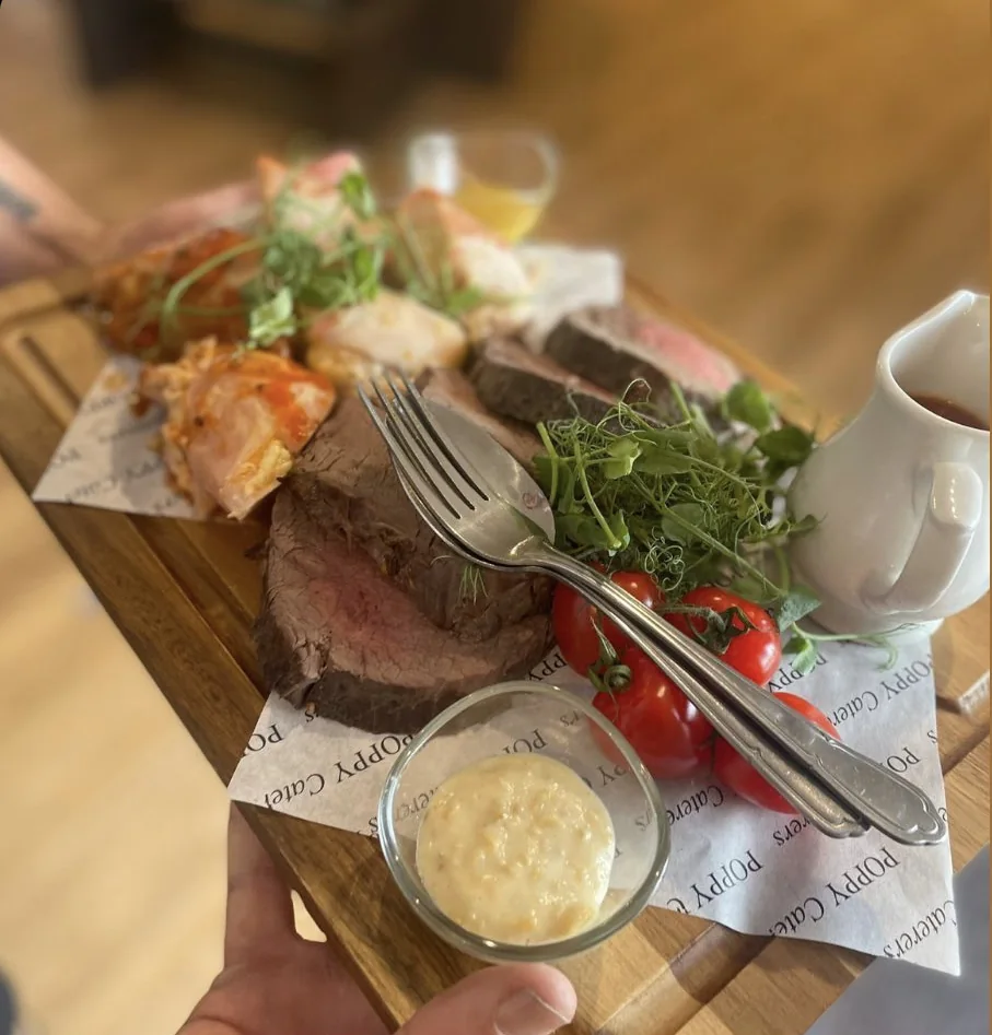 A sharing board with sliced meat, bread, salad and a small pot of butter.