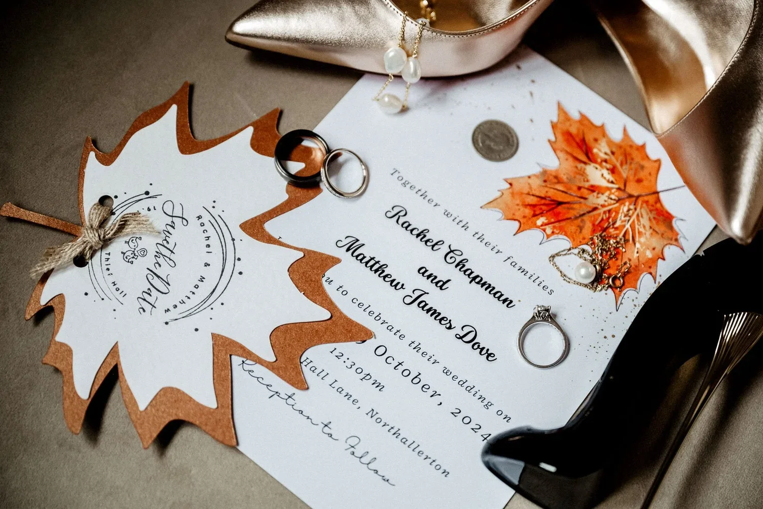 Autumn-leaf wedding invitations laid out with rings and bridal shoes.