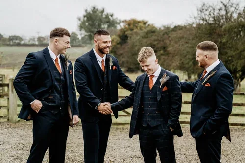 Four members of the wedding party laughing together in dark suits and orange ties.