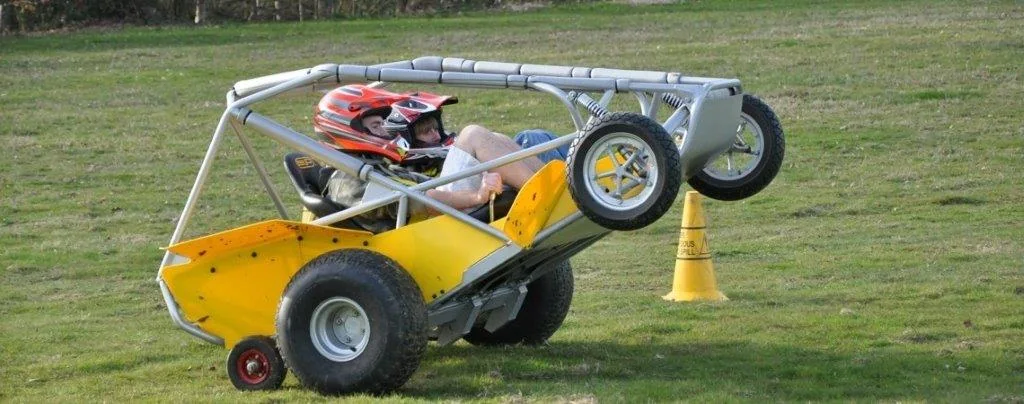 An off-road buggy taking a turn around a cone on grass.