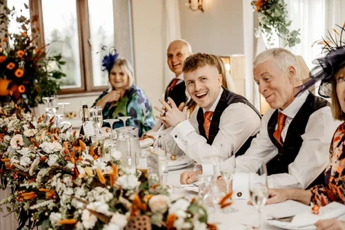 Guests laughing at a flower-decorated wedding reception table.