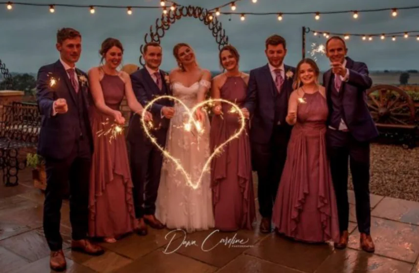 The newlyweds and their wedding party holding sparklers beneath festoon lights.