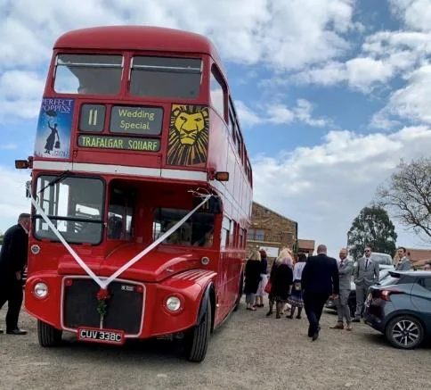 A red double-decker wedding bus parked outside the venue as guests gather.
