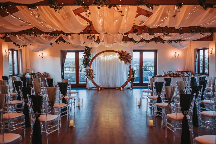 Clear ceremony chairs facing a circular arch beneath white Hall drapes