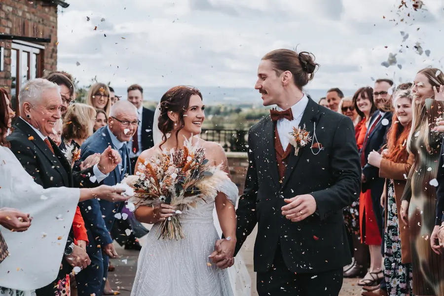 Confetti falling around the couple as guests line the courtyard