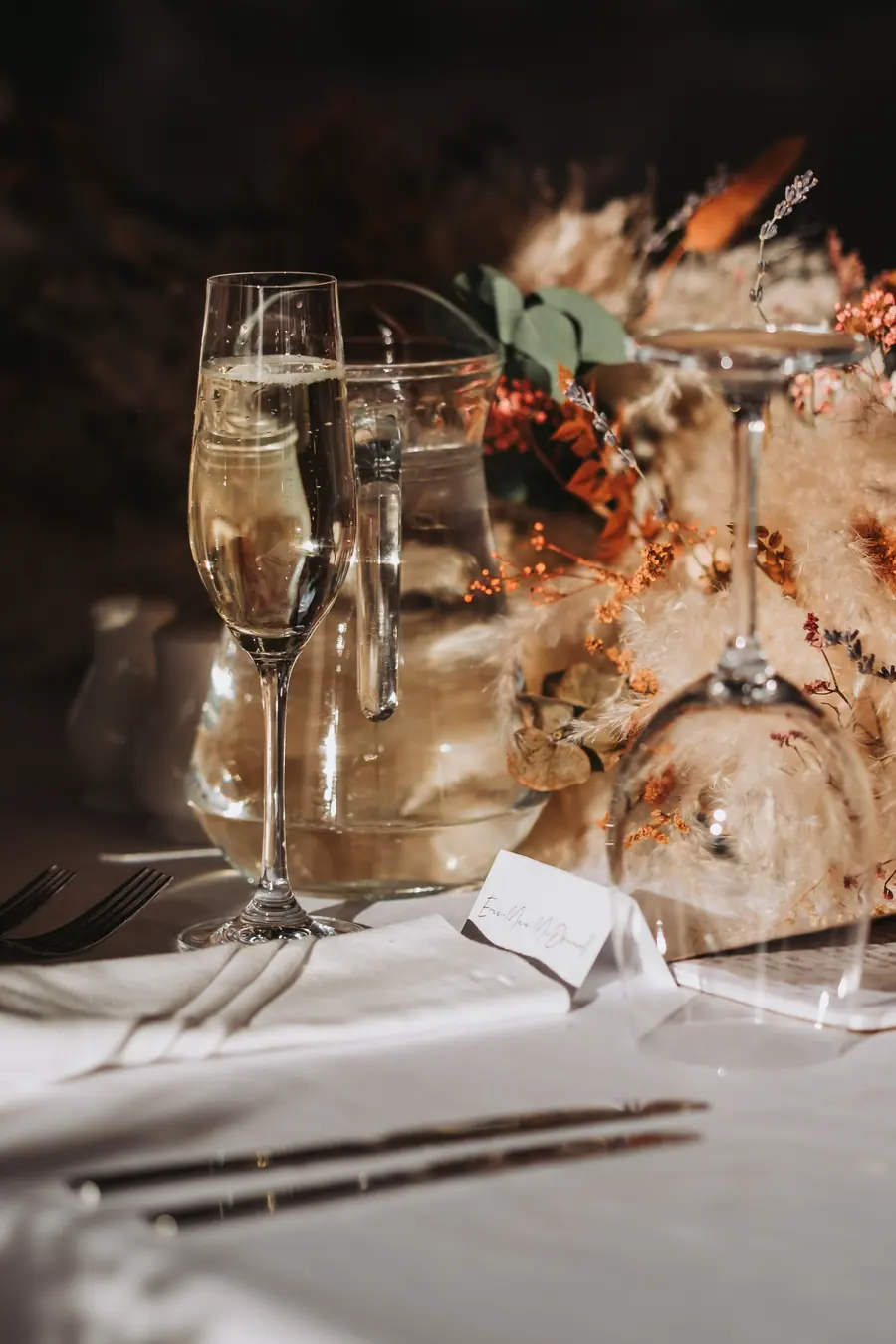 Champagne glasses beside dried flowers and rust fabric on a laid table