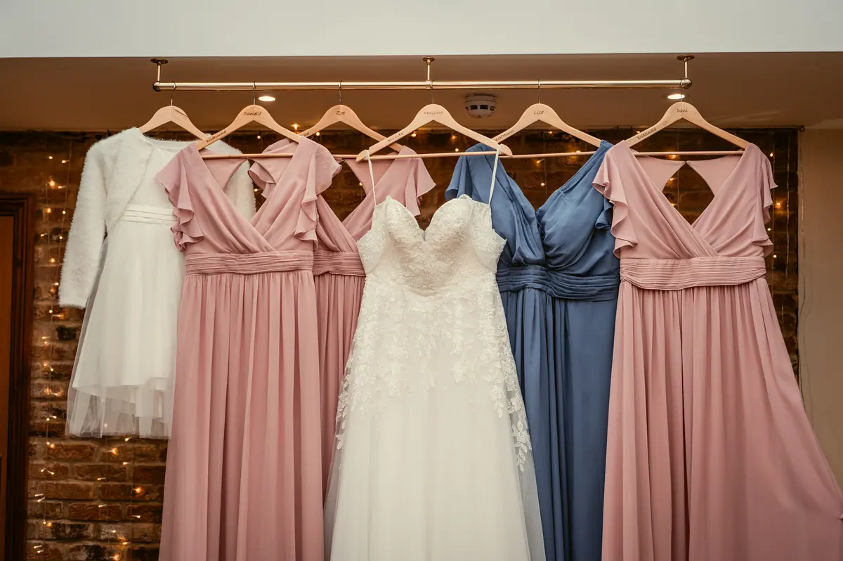 White wedding gown hanging between pink and blue dresses against wooden panelling