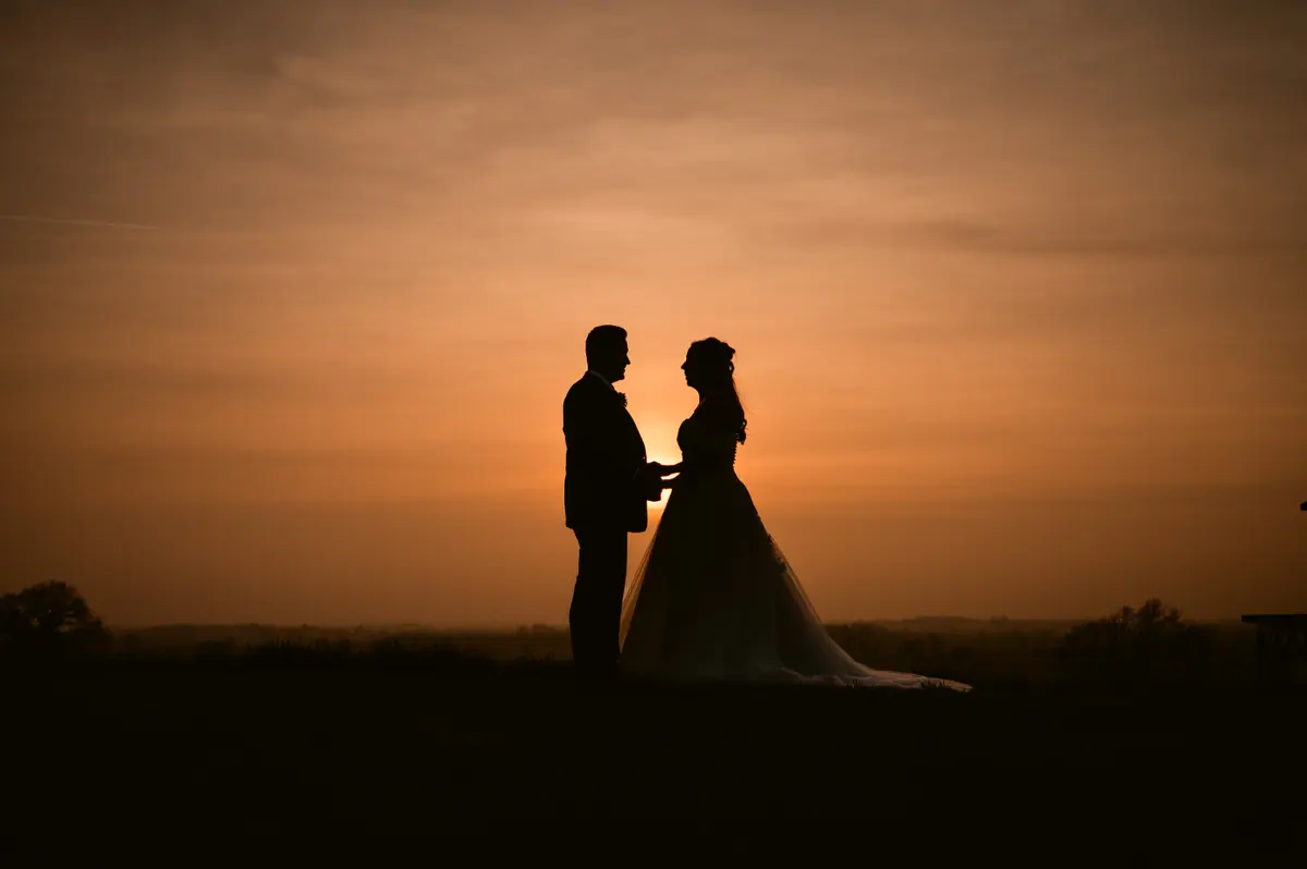 The couple standing in silhouette against a deep orange sunset