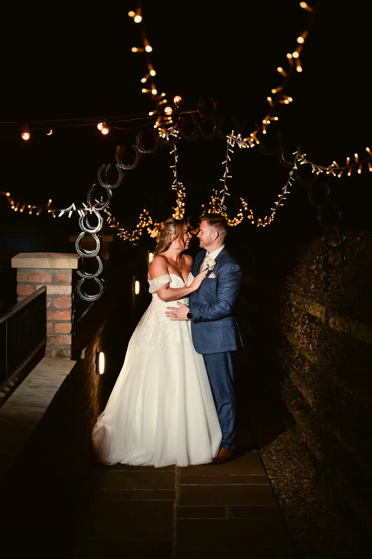 The couple embracing beneath warm lights on the stone terrace