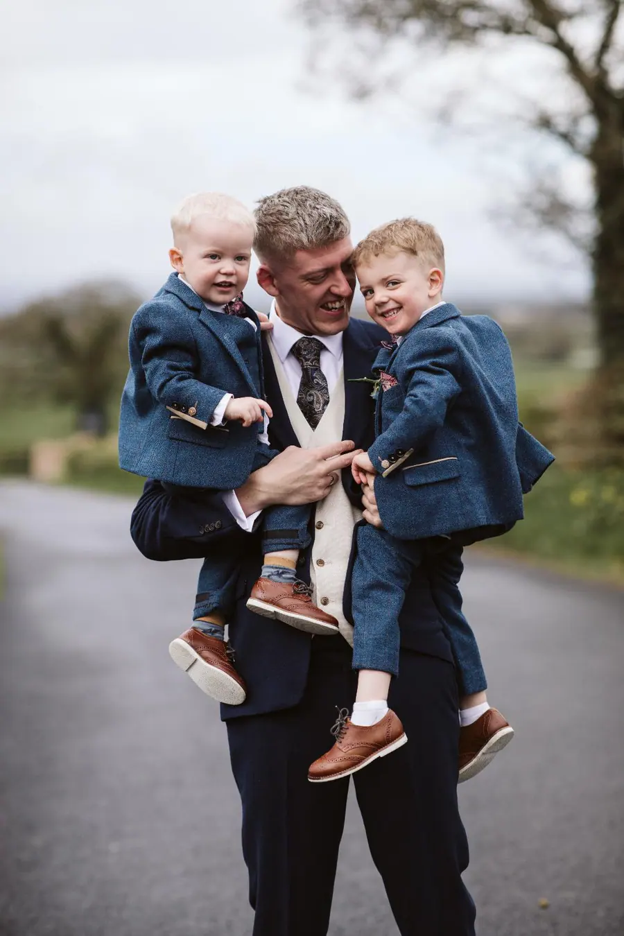 Jack carrying two young boys in matching blue suits along the lane