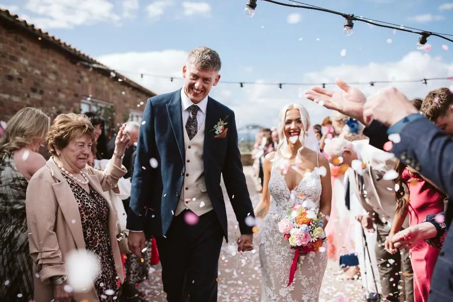 Guests throwing confetti as the couple leave the brick barns