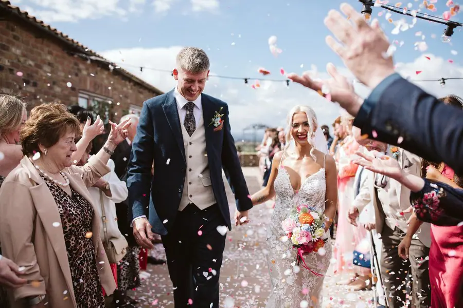 Confetti falling around the couple between two lines of guests