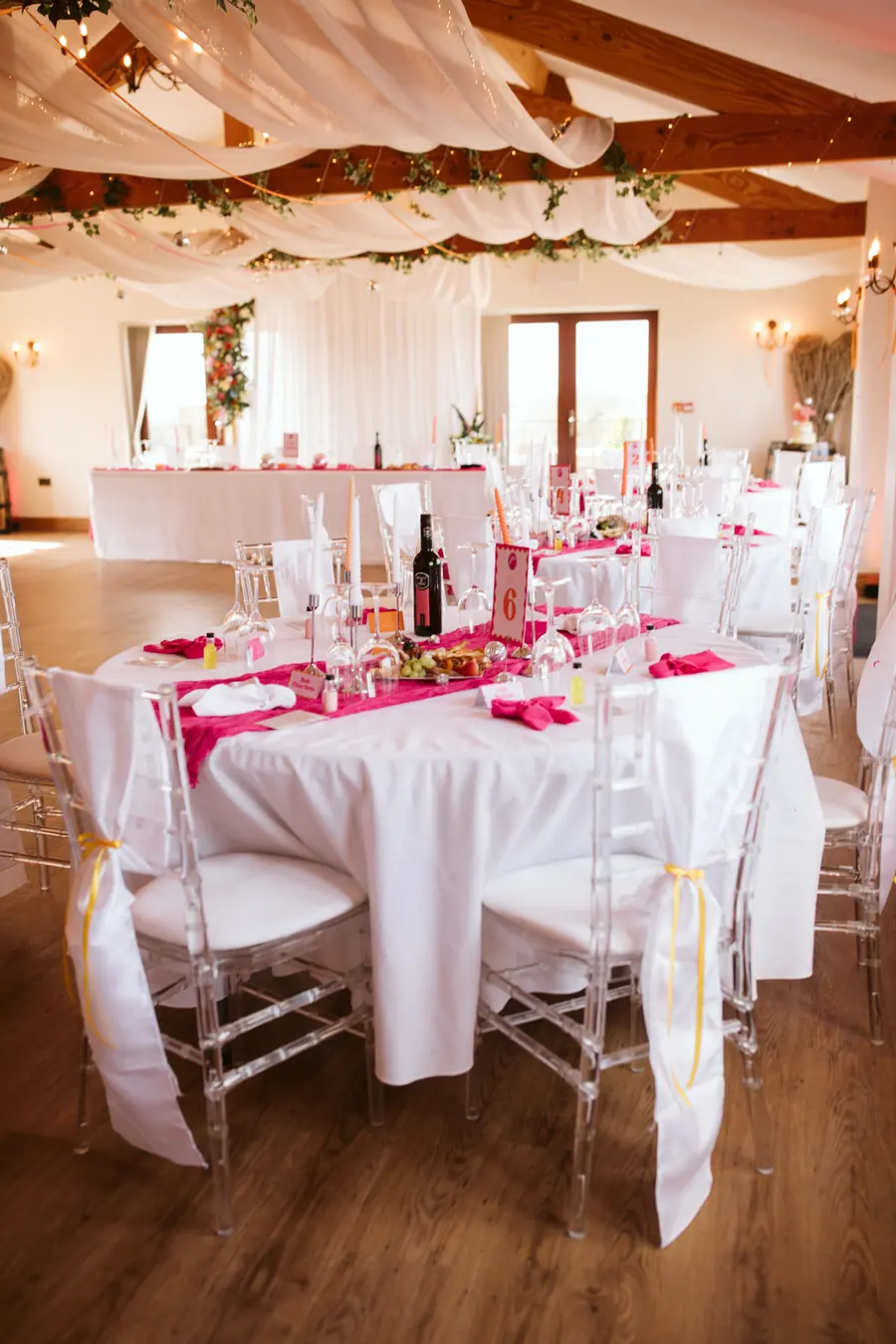 Hall tables dressed with bright pink napkins and clear chairs