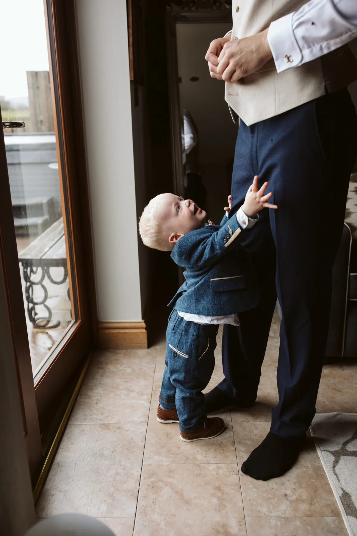 A young wedding guest reaching towards Jack as he gets ready by a window