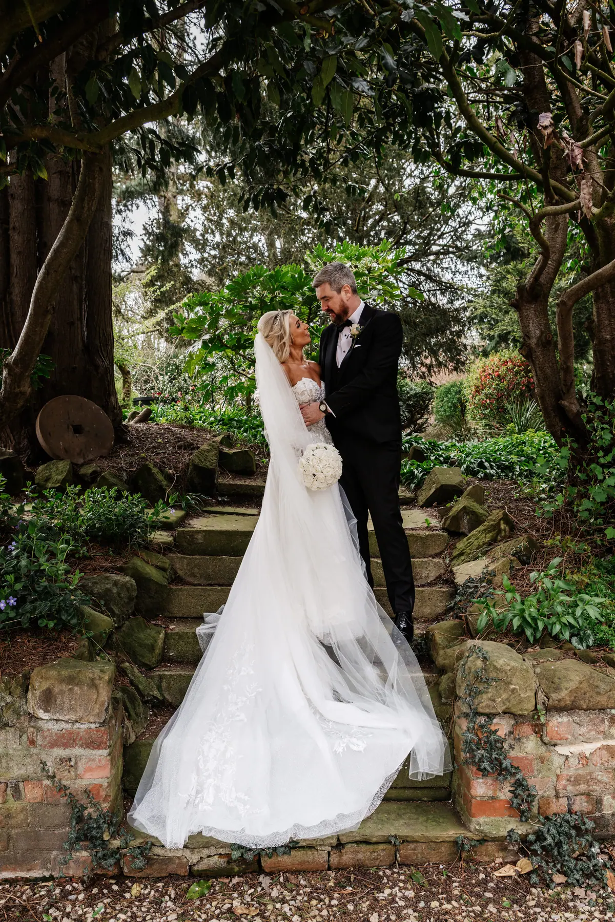 Jodie and Chris standing together on a stone path beneath trees