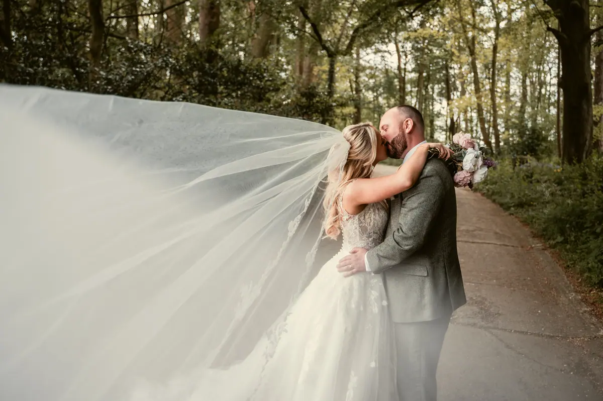 Katie's veil spreading behind the couple along a wooded lane