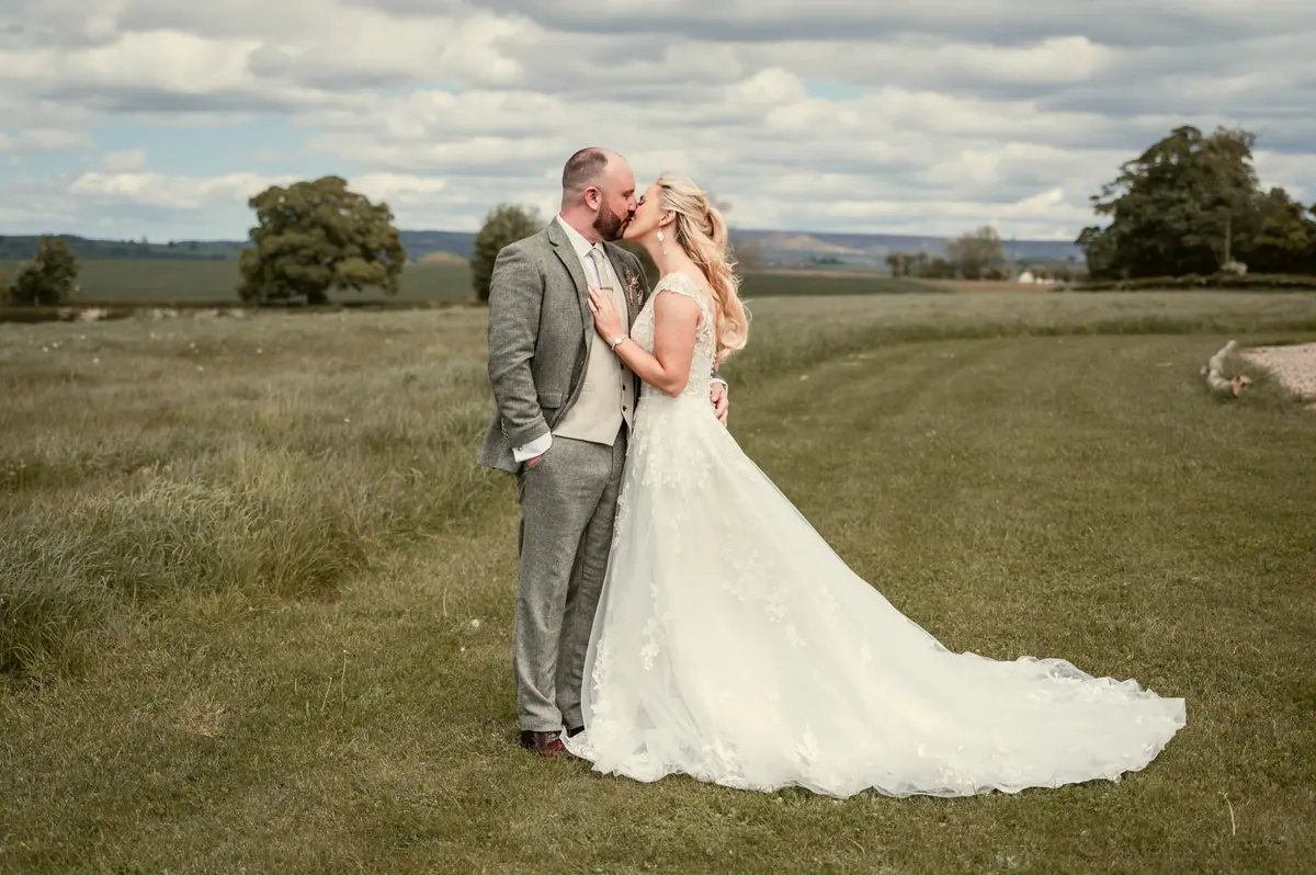 The couple embracing in a field with the venue grounds behind