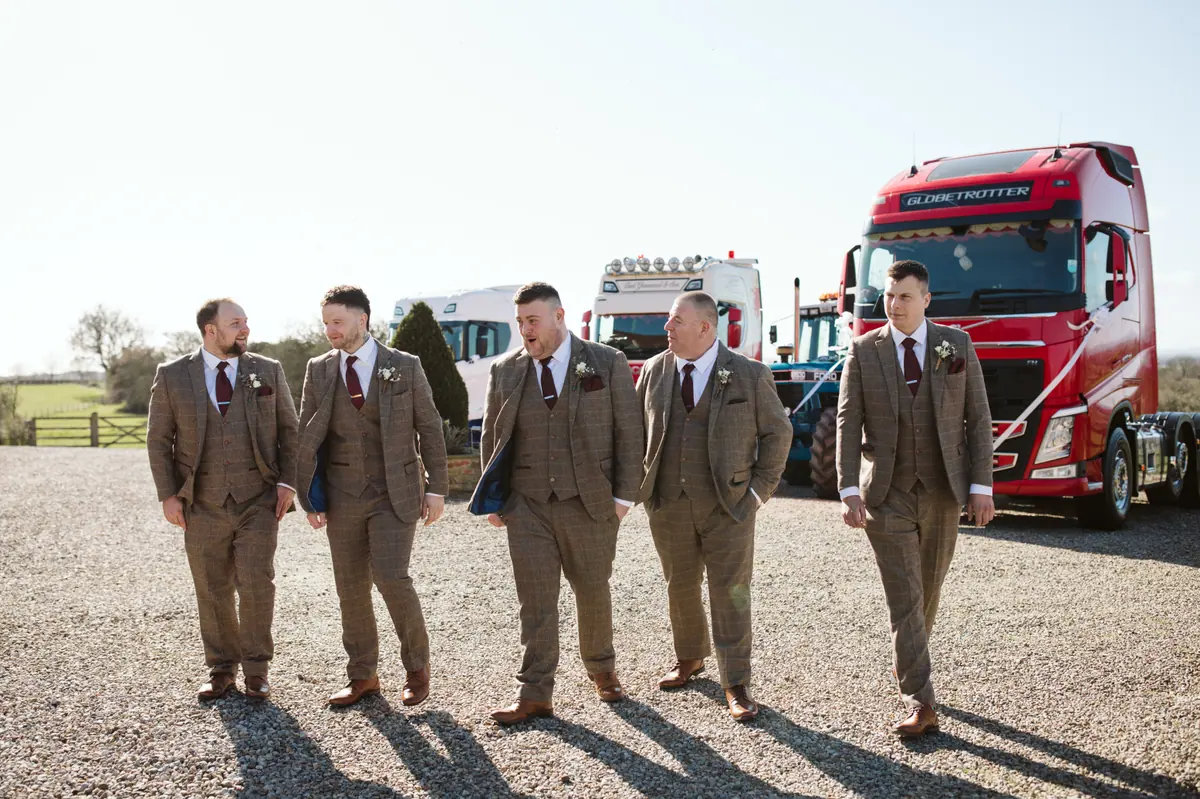 Six men in brown suits walking beside a bright red lorry