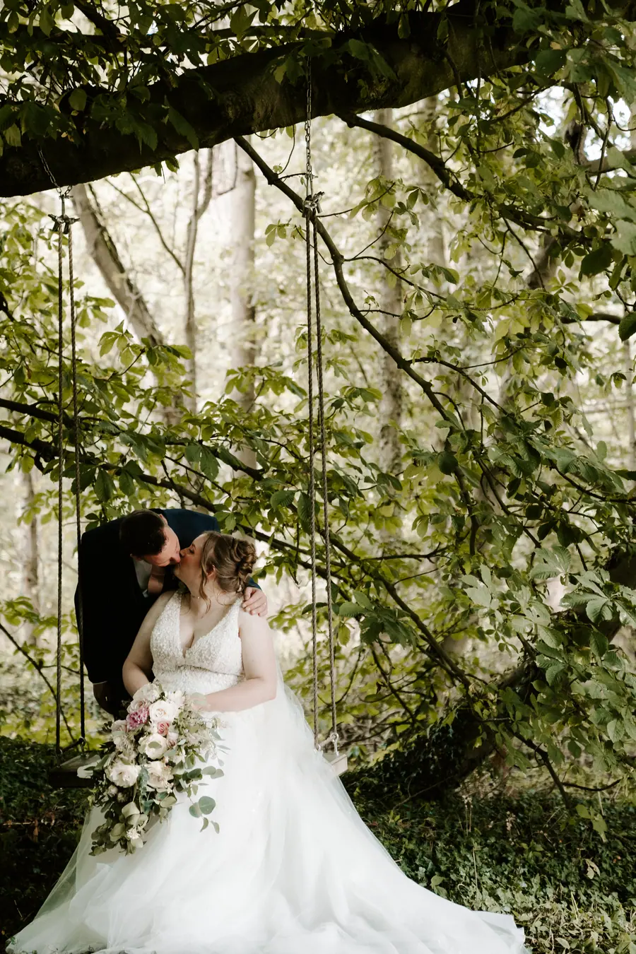 Laura and Marc kissing beneath low branches along the woodland path