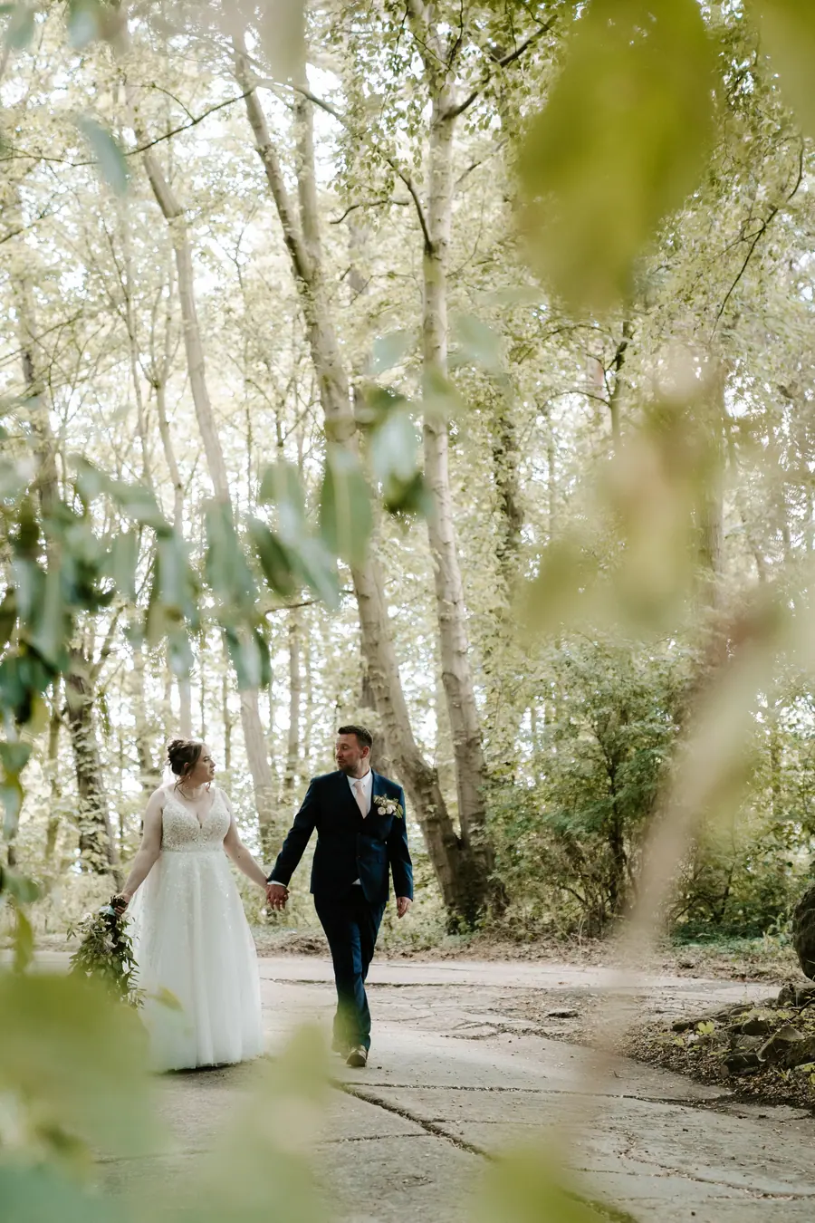 The couple walking hand in hand along the sunlit woodland path