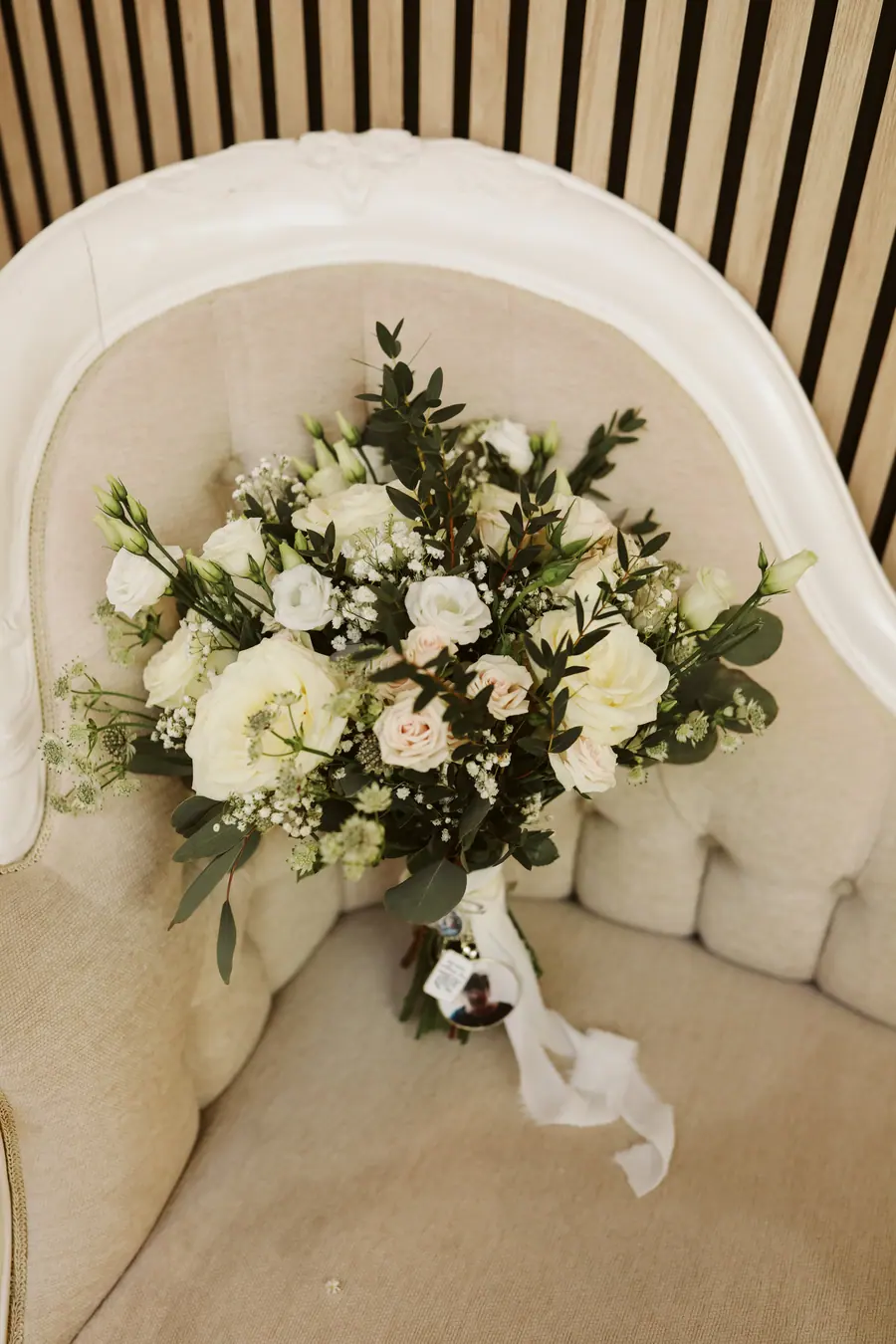White bridal bouquet resting on a curved cream ceremony chair
