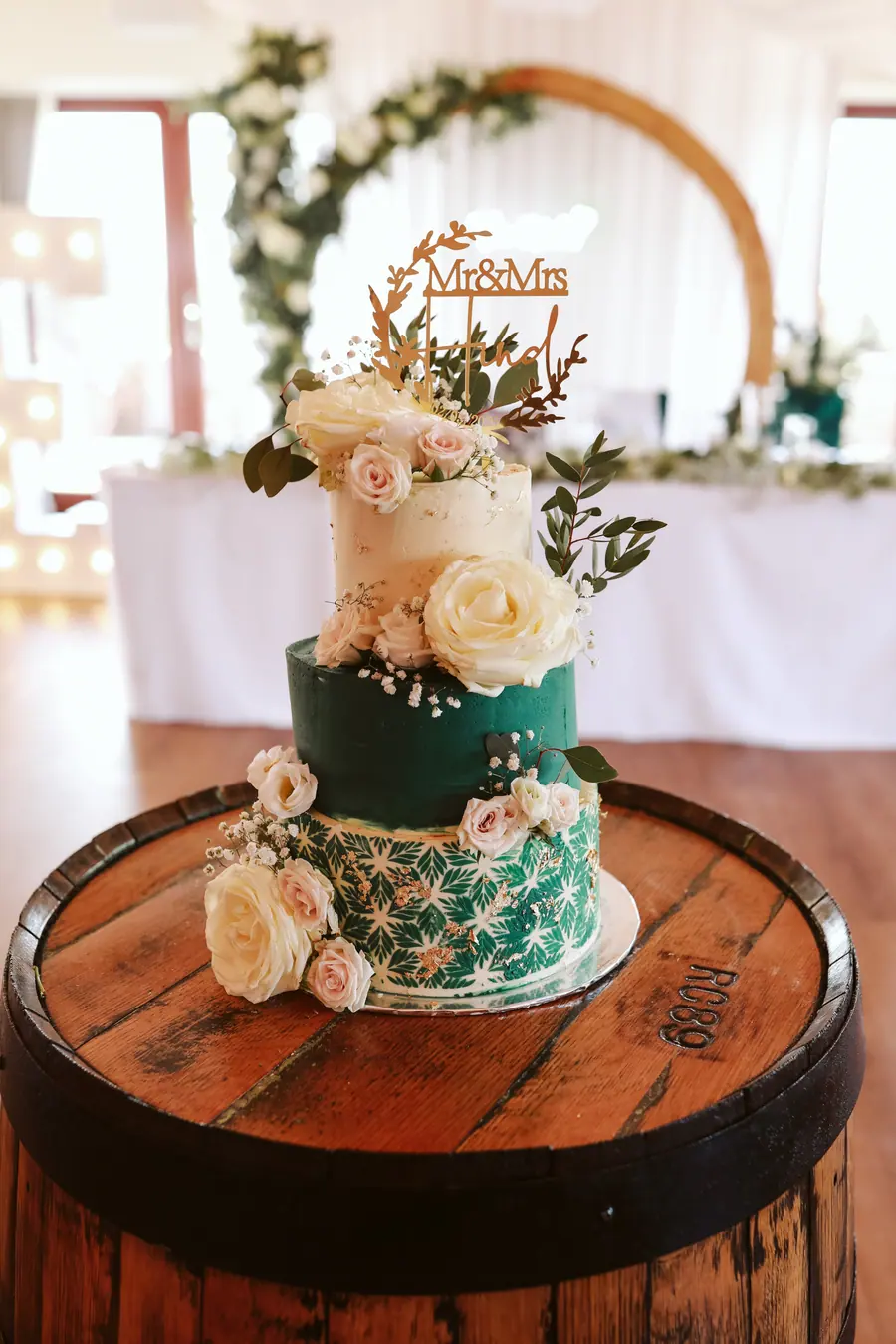 Green and cream tiered cake decorated with white flowers on a barrel