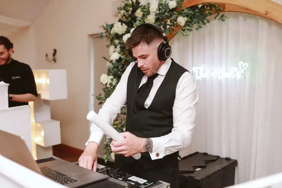 DJ wearing headphones behind his equipment beneath white drapes and greenery