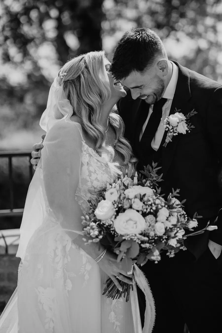 The couple standing close together with Lauren's white bouquet in black and white