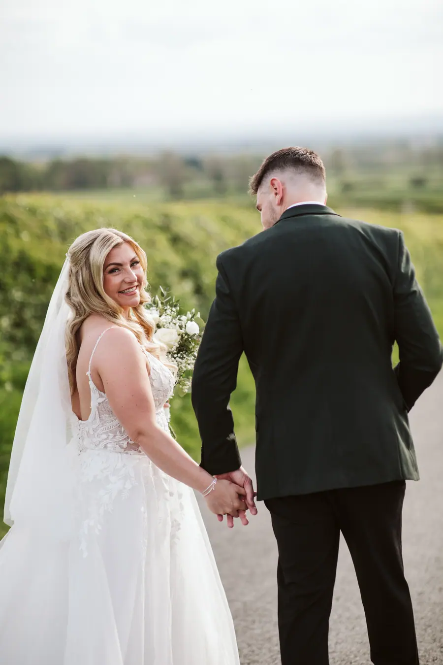 Lauren looking back while holding Iain's hand beside the fields