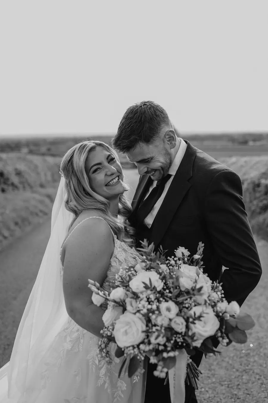 The couple looking down at the white bouquet in black and white