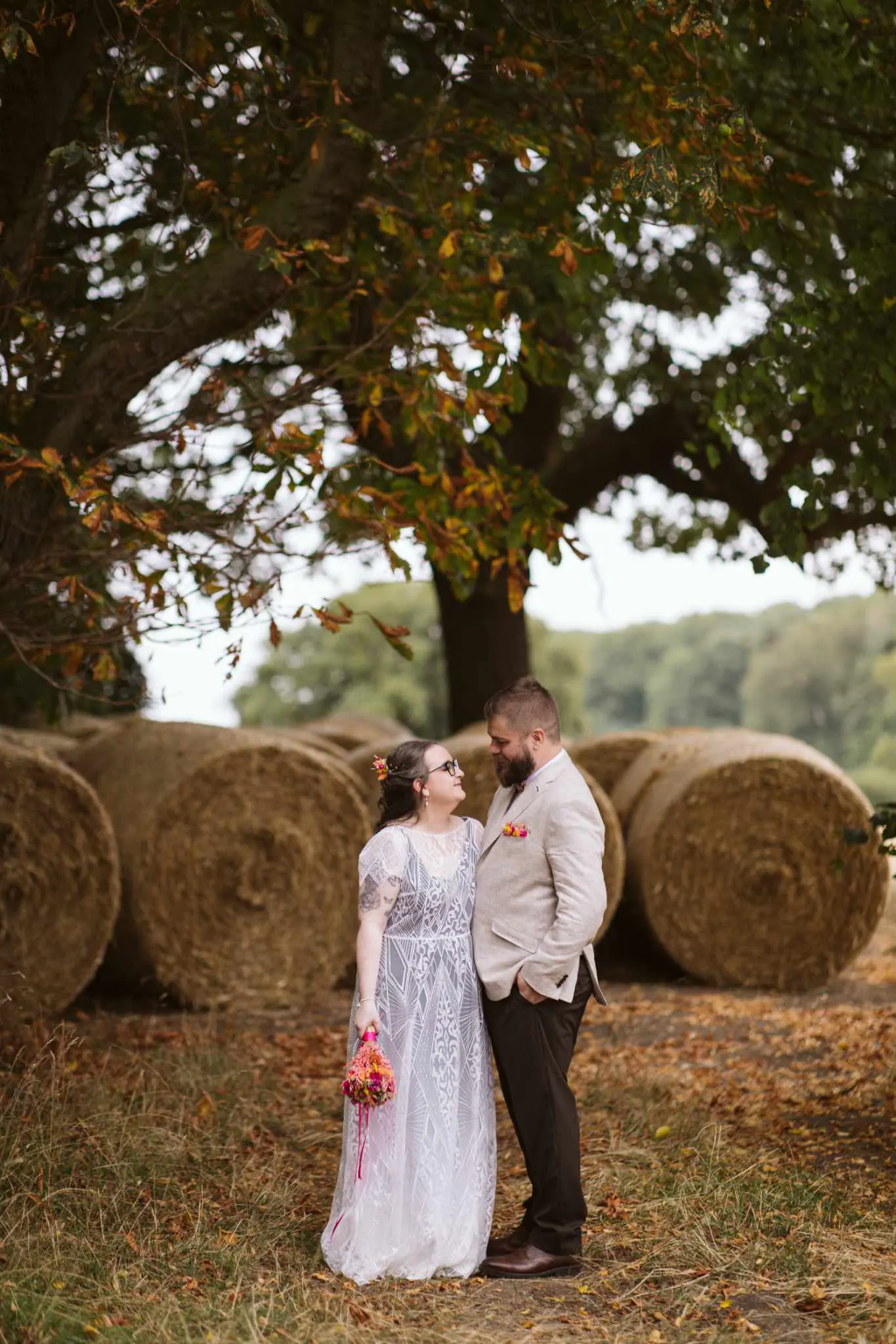 Lauren and Martin standing together beside round hay bales under a tree