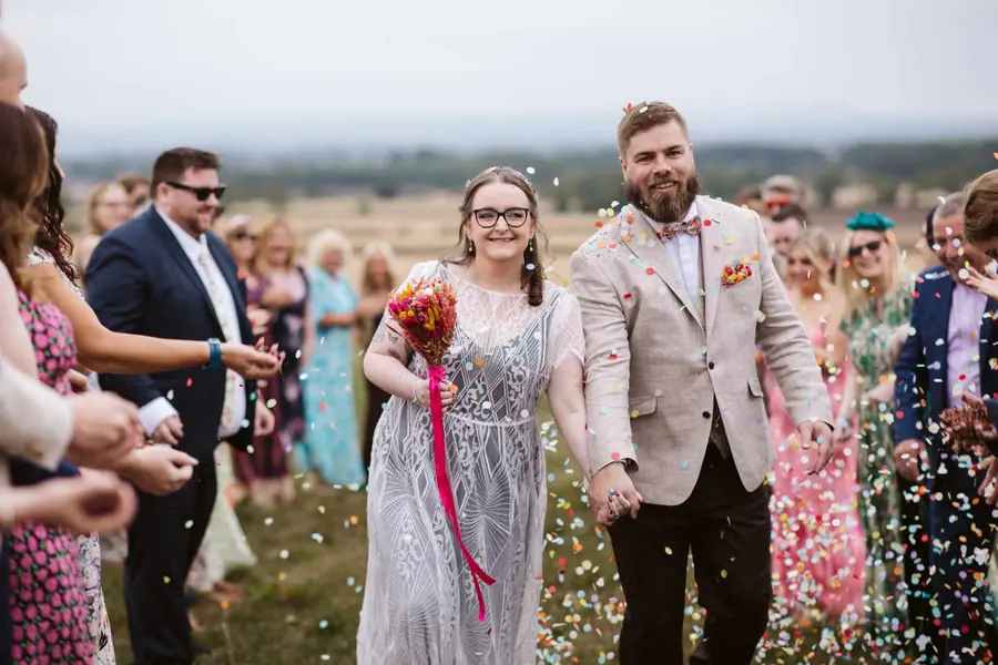 The couple walking through multicoloured confetti between two lines of guests