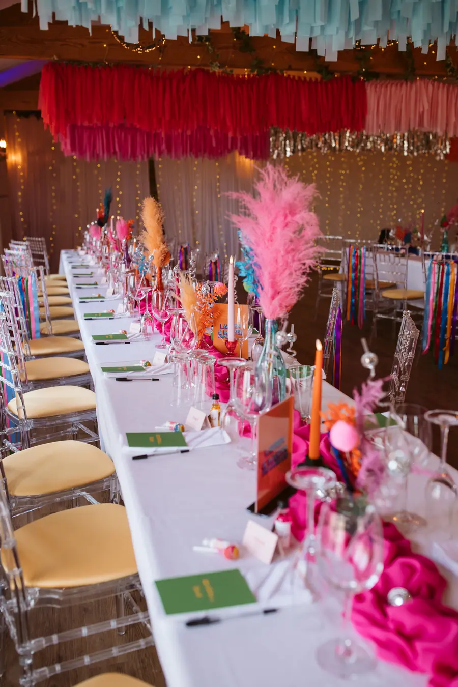 Dinner table filled with pink glassware, bright candles and coloured stationery